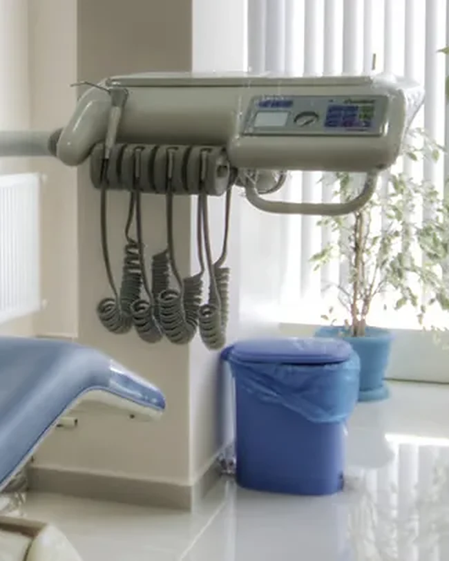 A dental instrument unit with hanging handpieces beside a treatment chair