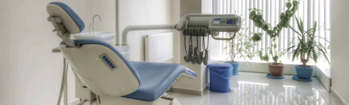 A dental treatment chair and instrument unit beside a window in a treatment room